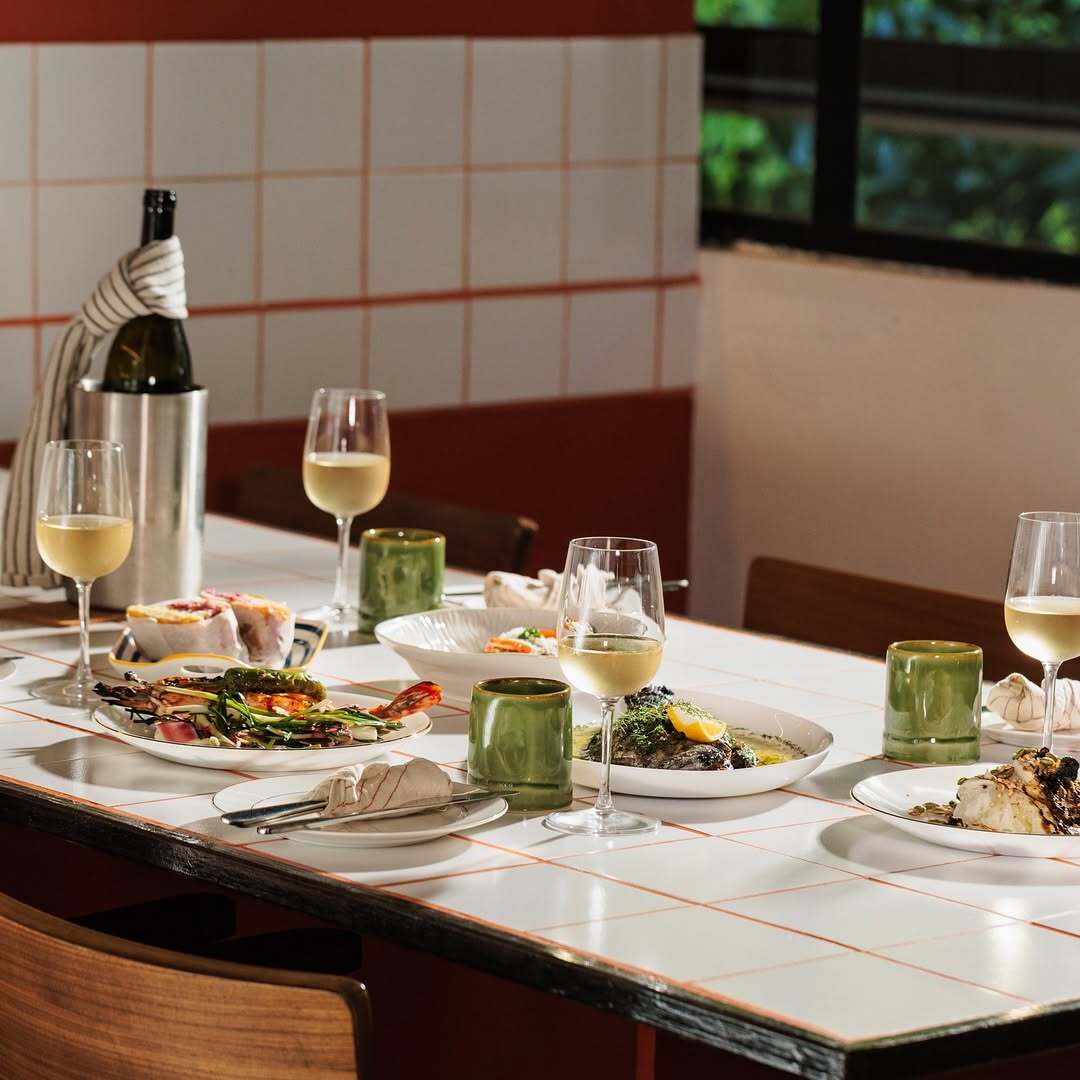 Table set with white wine, grilled prawn salad and whole fish in green herb sauce